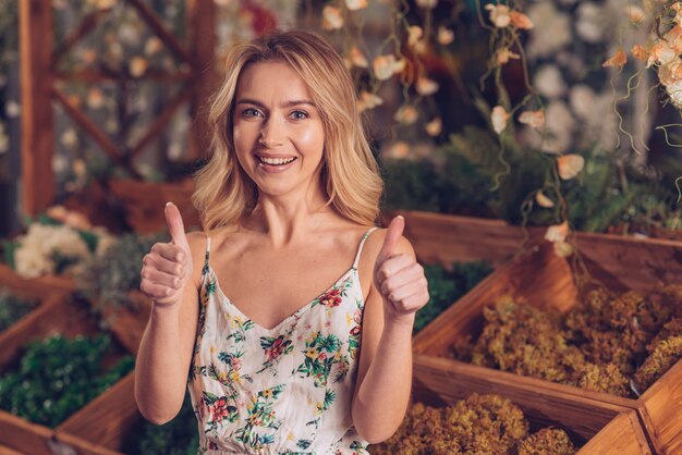 Portrait of a blonde young female florist showing thumb up sign with two hands
