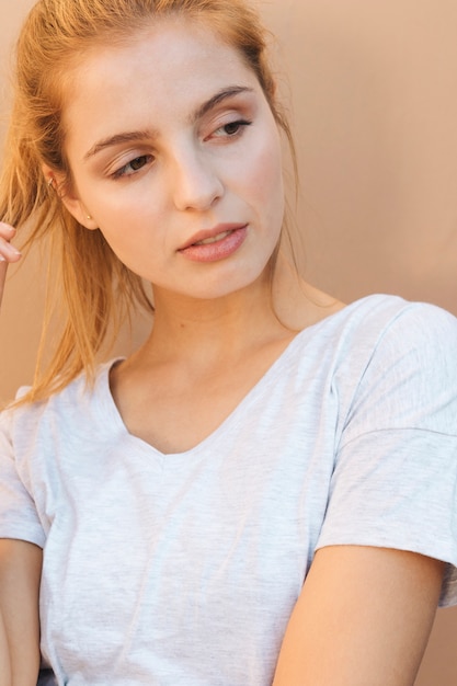 Free photo portrait of a blonde young woman looking away against beige backdrop