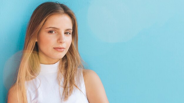 Portrait of a blonde young woman looking at camera against blue background