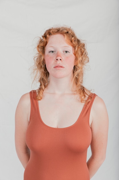 Free photo portrait of a blonde young woman looking at camera against grey wall