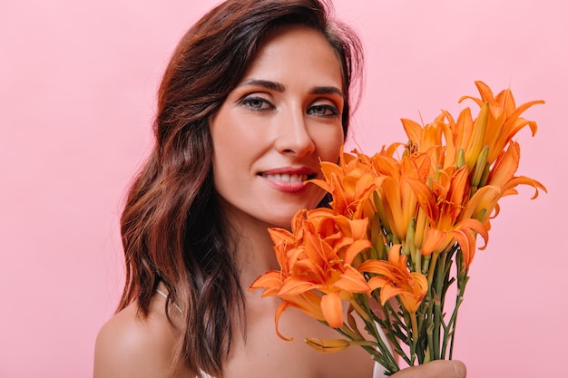 Portrait of blue-eyed woman with orange flowers in her hands. Photo of dark-haired girl with beautiful smile with big bouquet.