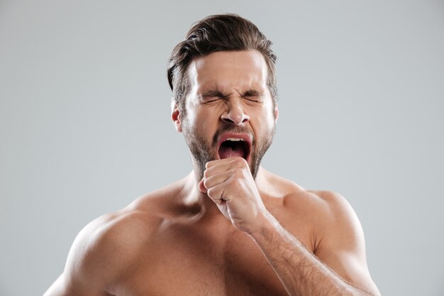 Portrait of a bored beraded man with naked shoulders yawning