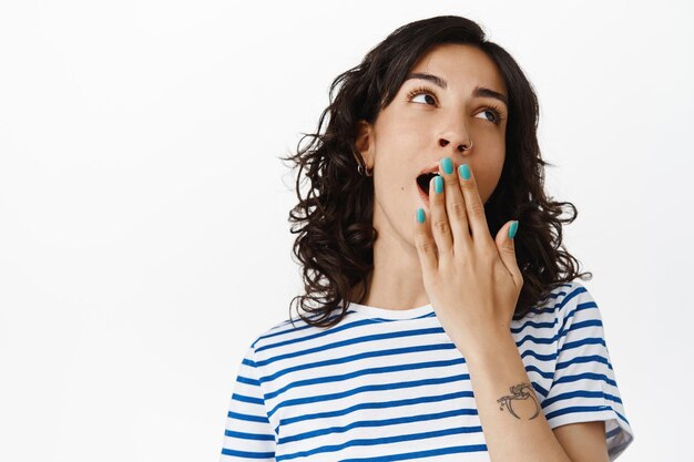 Portrait of bored brunette girl, look away and yawning with tired face, watching boring movie, standing in t-shirt against white background