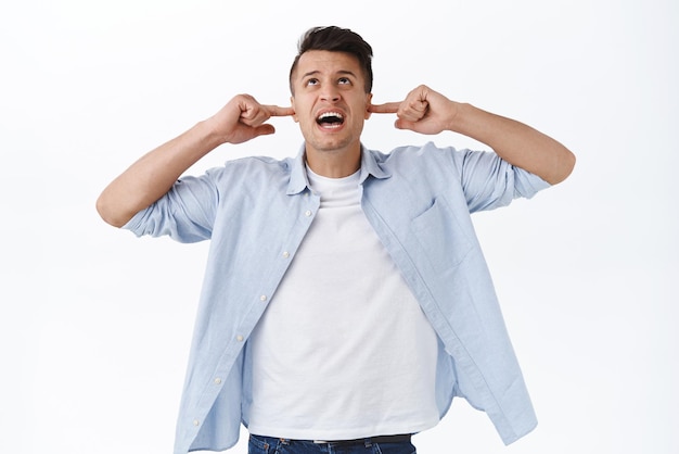 Free photo portrait of bothered and annoyed handsome man hate his neighbours shut ears and look up shouting people upstairs to turn music off roommate being too loud cant stand noise