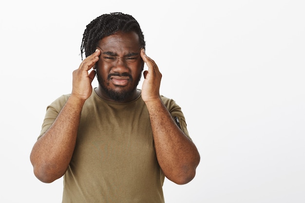 Portrait of bothered guy in a brown t-shirt posing against the white wall