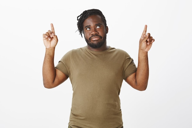 Портрет обеспокоенного парня в коричневой футболке, позирующего у белой стены