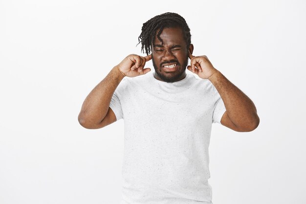 Portrait of bothered guy with braids posing against the white wall