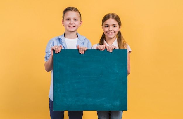 男の子と女の子黄色の背景に対して立っている緑の黒板を保持の肖像画