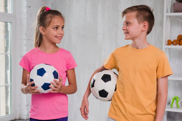 Portrait of a boy and girl holding soccer balls in hand looking at each other