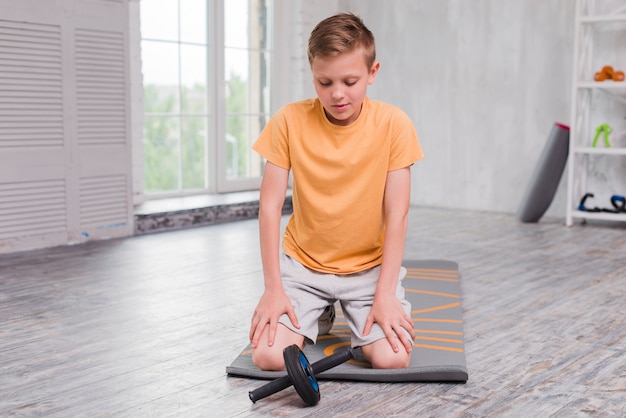 Free photo portrait of a boy kneeling on exercise mat looking at roller slide