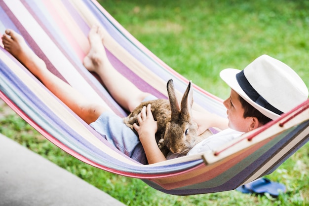 Portrait of boy lying on hammock with rabbit in hand