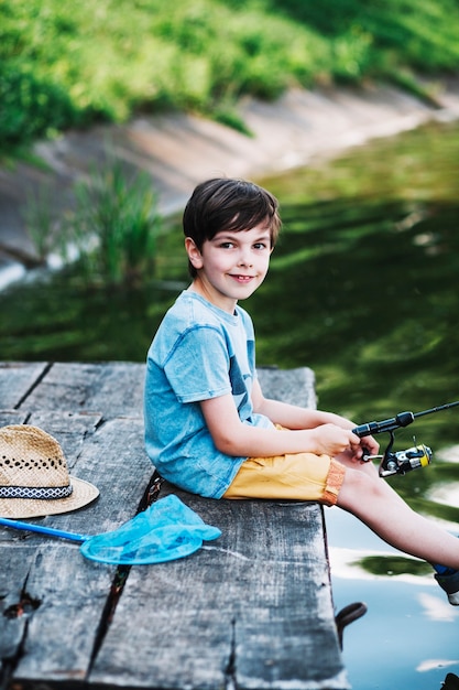 Free photo portrait of boy sitting on pier fishing on lake