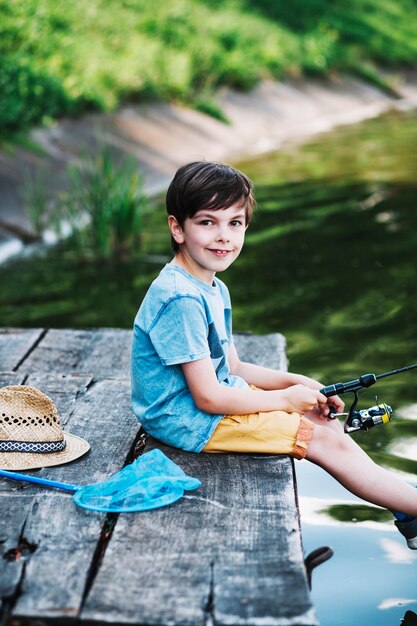 Portrait of boy sitting on pier fishing on lake