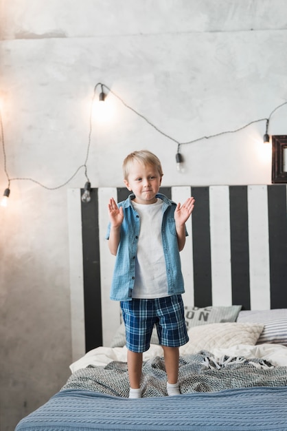 Foto gratuita ritratto di un ragazzo in piedi sul letto con luce illuminata sul muro