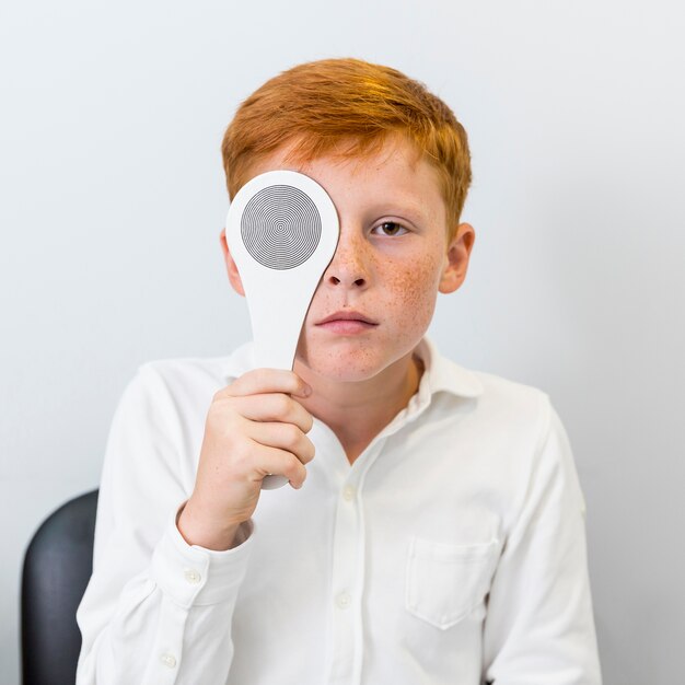Portrait of boy with freckle holding occluder in front of his eye