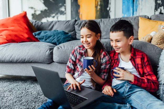 Portrait of brother and sister watching funny movie with cup of juice, while using laptop.