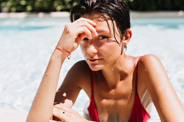 Portrait of brown-haired woman with tanned skin relaxing in pool.