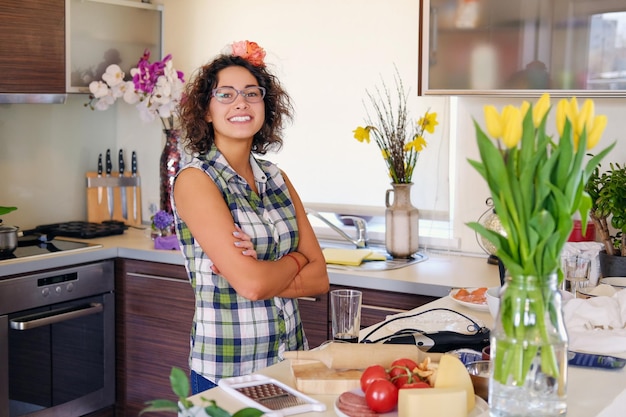 Portrait of brunette attractive female with curly hair in a home kitchen with a lot of flowers.