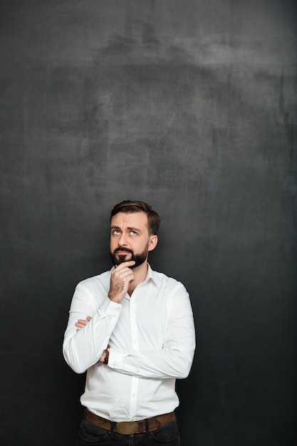 Портрет брюнетки Бородатый мужчина в белой рубашке, касаясь его подбородка, думая или вспоминая над темно-серым