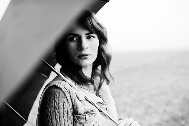 Portrait of brunette curly girl in jeans jacket with black umbrella at field