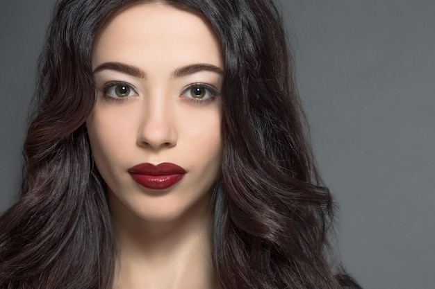 Portrait of brunette fashion model woman with dark red lips in studio. Beautiful lady with perfect make-up and skincare posing for fashion magazine.