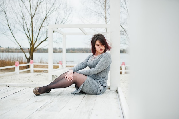 Free photo portrait of brunette girl in gray dress sitting at white wooden construction