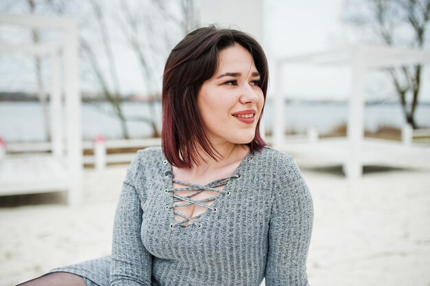 Portrait of brunette girl in gray dress sitting at white wooden construction