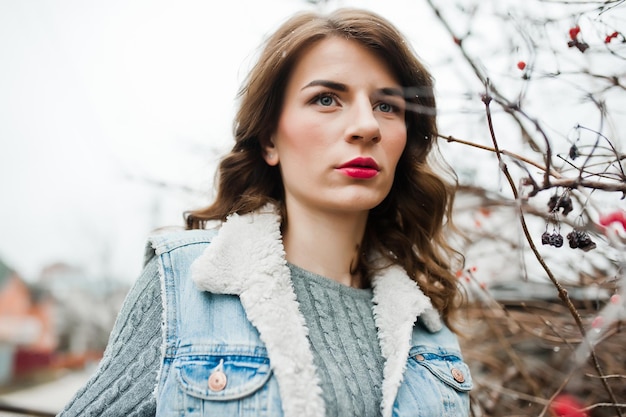 Portrait of brunette girl in jeans jacket at frozen bushes