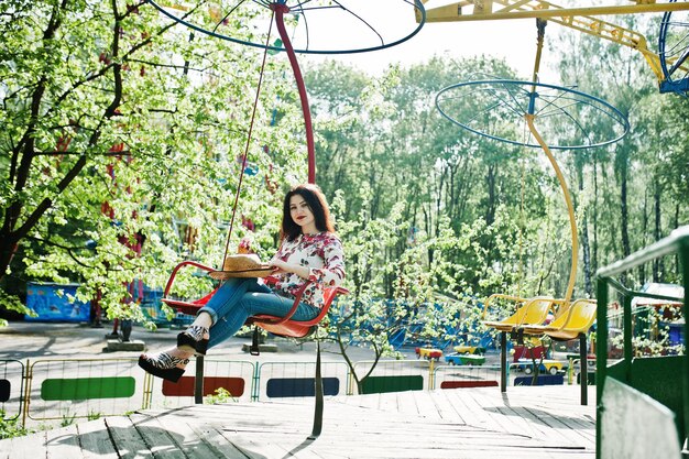 Portrait of brunette girl in pink glasses and hat with ice cream at amusement park