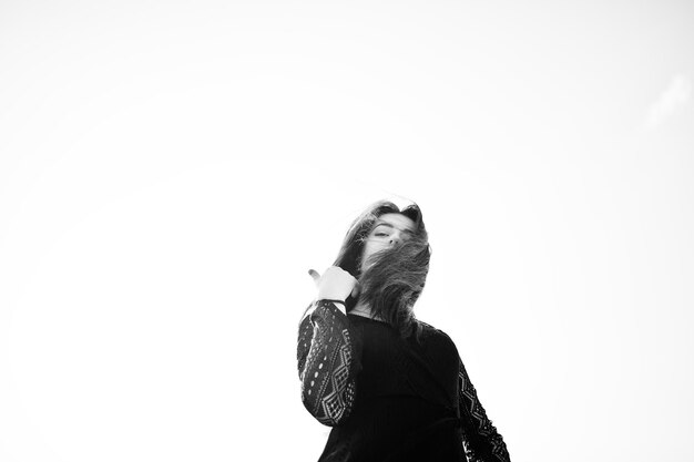 Portrait brunette girl with red lips wearing a black dress posed against blue sky on sunny day