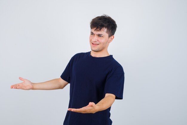 Portrait of brunette man making asking question gesture in dark t-shirt and looking thoughtful.