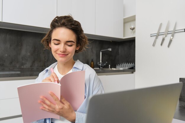 Portrait of brunette woman does homework works from home prepares for exam in kitchen sits with