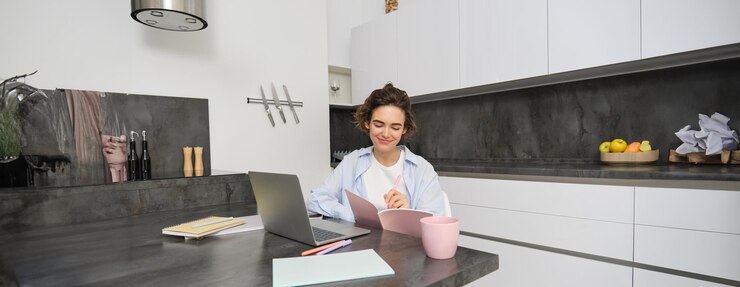 मुफ़्त फोटो portrait of brunette woman does homework works from home prepares for exam in kitchen sits with