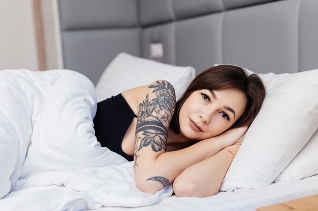 Portrait of brunette woman lie on the bed in the morning wake up stretching her arms and body