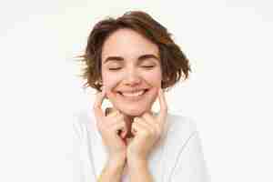 Free photo portrait of brunette woman smiling shuts her eyes and touches dimples on her cheeks stands over