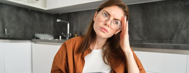 Portrait of brunette woman working from home wearing glasses looking concerned touching head and