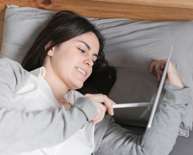 Foto gratuita ritratto della donna castana che lavora alla compressa a letto