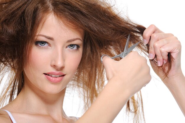 Portrait of brunette young woman cutting her hair isolated on white