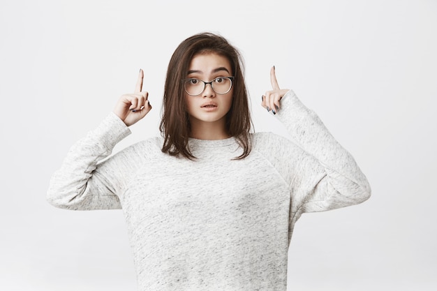 Portrait of brunette young woman in glasses pointing up