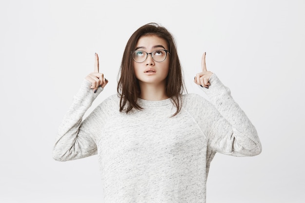 Portrait of brunette young woman in glasses pointing up