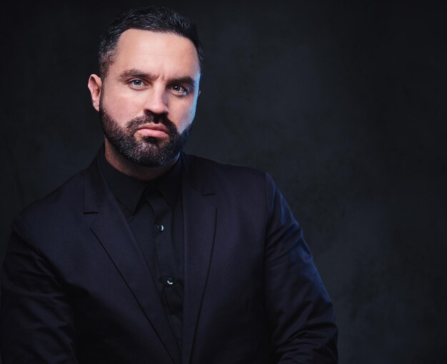 Portrait of brutal bearded macho male dressed in a suit over dark grey background.