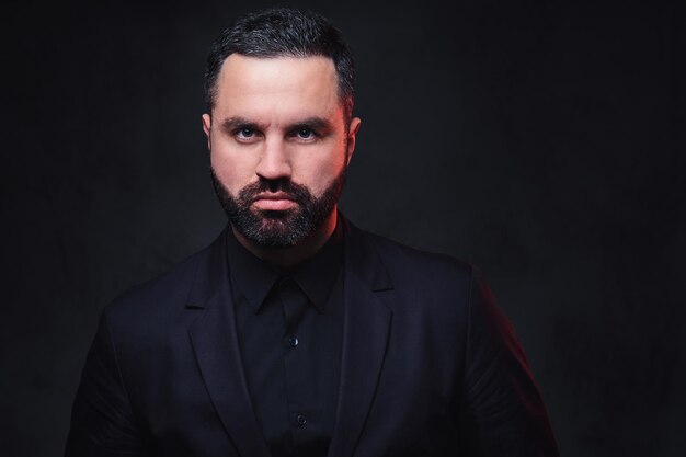 Portrait of brutal bearded macho male dressed in a suit over dark grey background.