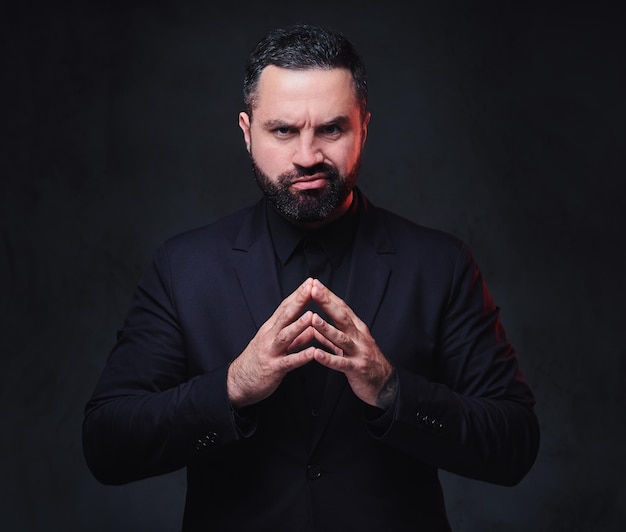 Portrait of brutal bearded macho male dressed in a suit over dark grey background.