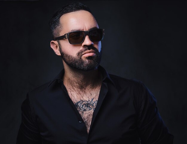 Portrait of brutal bearded male in sunglasses with tattoos on arms and neck.