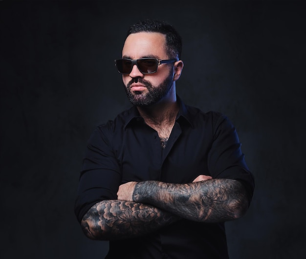 Portrait of brutal bearded male in sunglasses with tattoos on arms and neck.