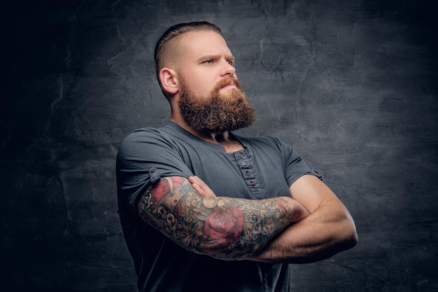 Portrait of brutal bearded male with tattooed crossed arms.