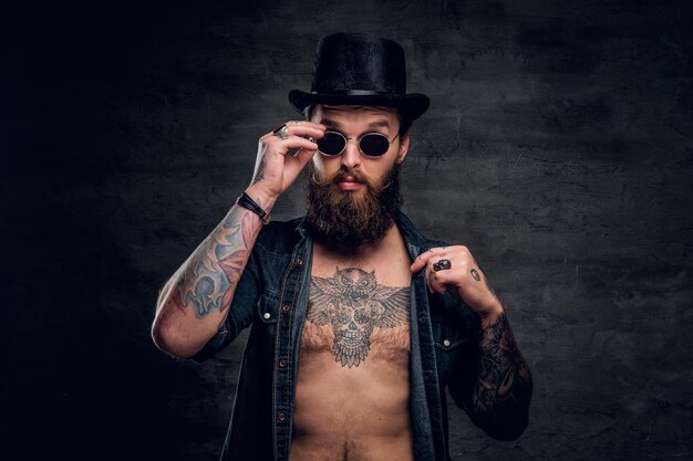 Portrait of brutal man with open denim shirt and tattooed chest.