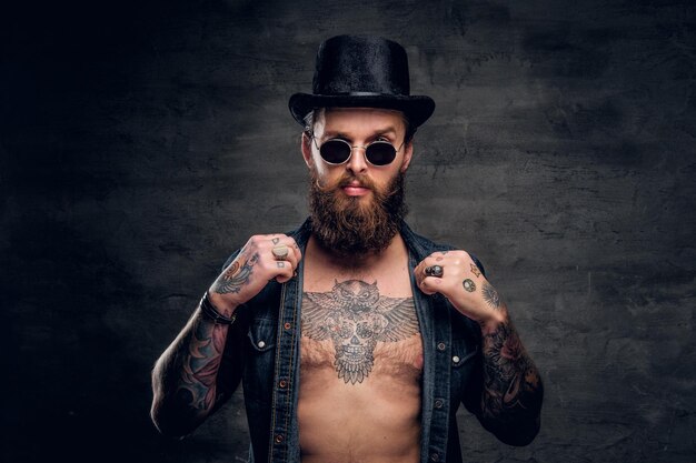 Portrait of brutal man with open denim shirt and tattooed chest.