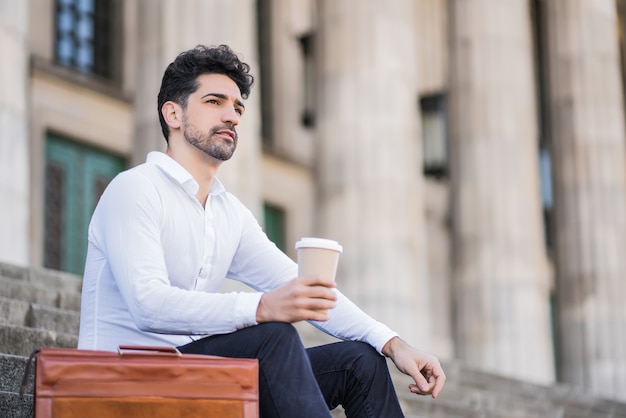 야외 계단에 앉아있는 동안 직장에서 휴식 시간에 커피 한 잔을 마시는 비즈니스 남자의 초상화