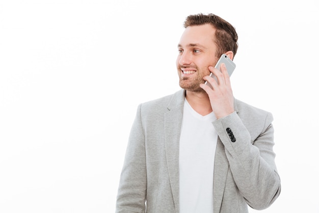 Portrait of businesslike guy in jacket having pleasant mobile conversation using cellphone and looking aside